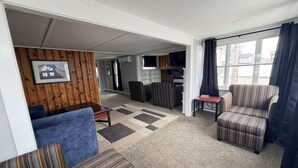 A living room with a blue sofa, striped armchairs, a coffee table, and a rug. There is a kitchen area with a refrigerator and cabinets in the background. - Walk to Lake • Strip • Wineries • Firepit (Geneva)