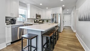 Una cocina moderna con armarios blancos, electrodomésticos de acero inoxidable y una isla central con taburetes.