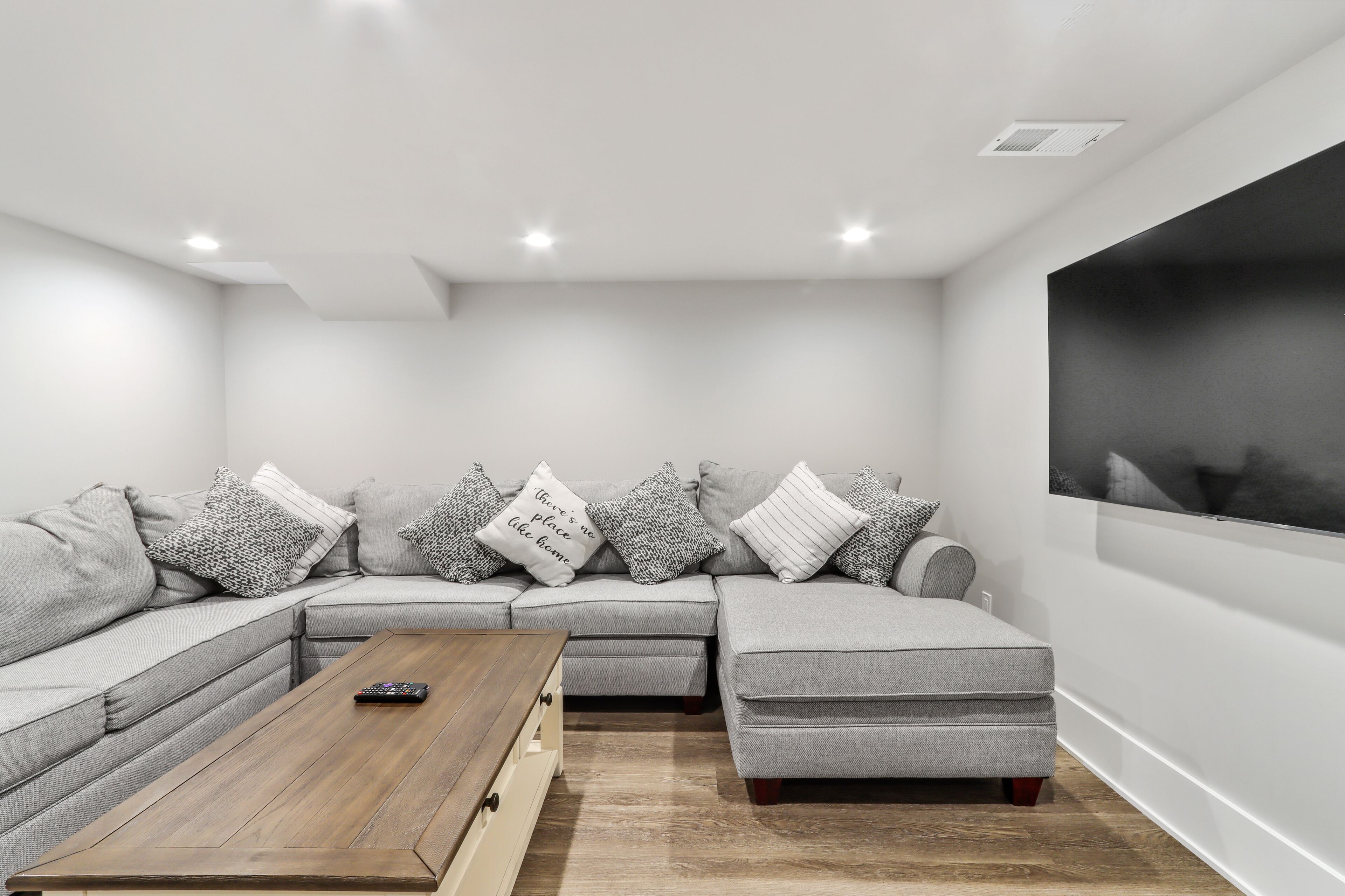 A modern living room with a sectional sofa, a coffee table, and a large wall-mounted TV.