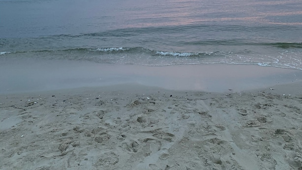 Una playa con huellas y un atardecer sobre el océano.