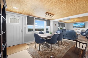 A modern kitchen with a dining area, a seating area with leather chairs, and a large TV mounted on the wall.