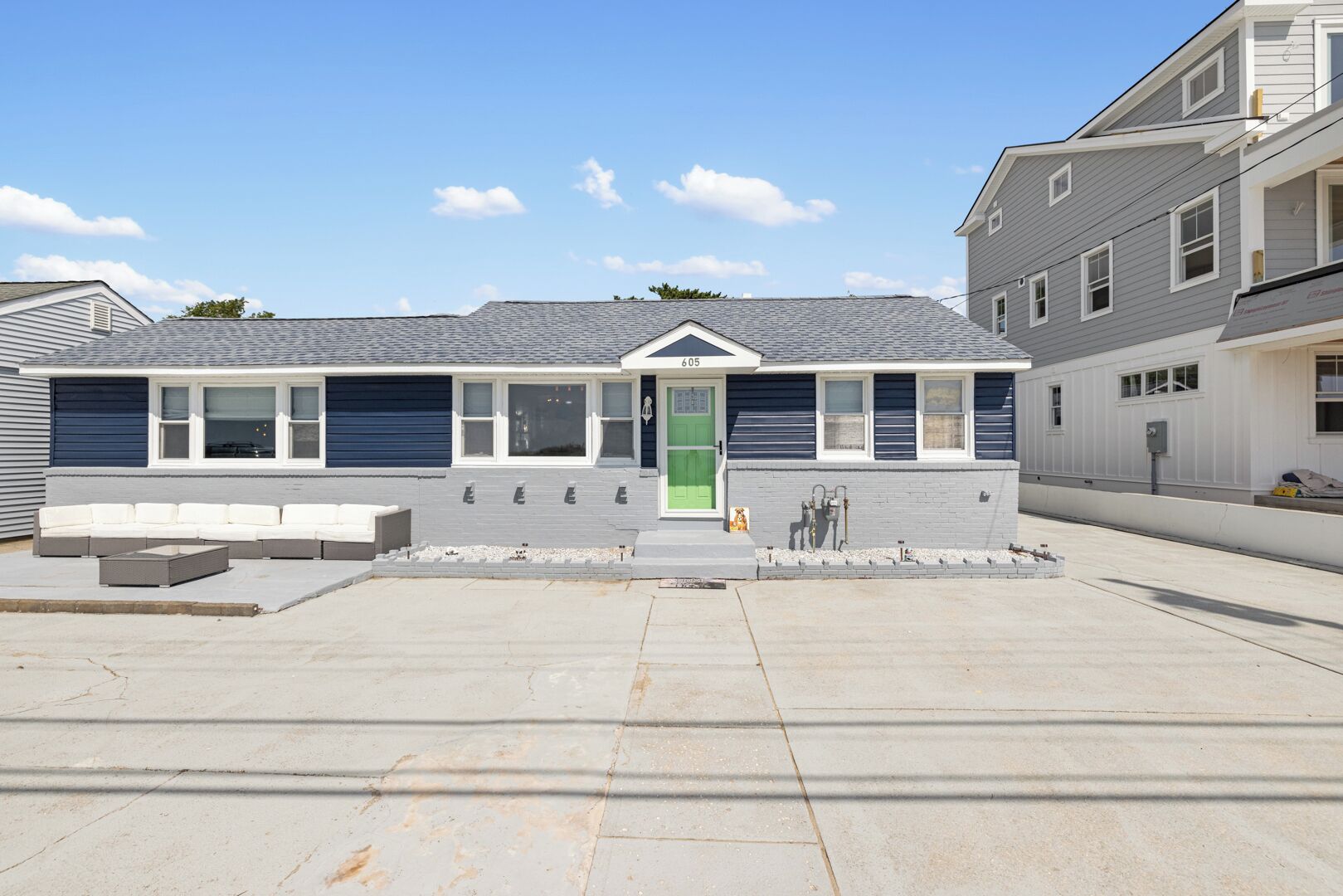 Un bâtiment moderne à deux étages, avec une façade grise, une porte verte et un espace extérieur abrité avec des sièges.
