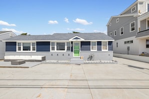 A modern two-story building with a grey exterior, a green door, and a covered outdoor seating area.