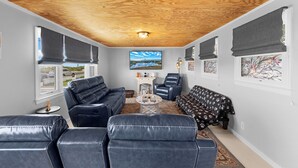 Un espacio habitable compacto con techo de madera, un sofá de cuero negro, un sofá estampado, un sillón reclinable y obras de arte en las paredes.
