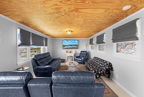 A compact living space with a wooden ceiling, a black leather sofa, a patterned sofa, a reclining chair, and artwork on the walls.