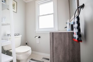 Un baño con inodoro blanco, ventana, toallero y zona de ducha.