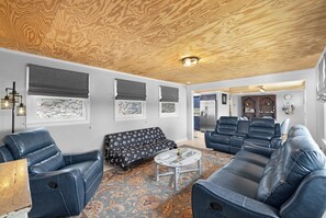 A modern living room with leather sofas, a patterned rug, and a wooden ceiling.