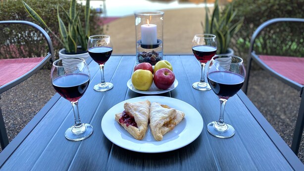 A table set with wine glasses, fruits, a candle, and pastries, overlooking a body of water. - Spoil yourself with this beautiful Lake Balboa retreat (Hot Springs Village)