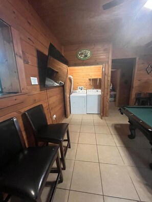Ein Zimmer mit Billardtisch, Waschmaschine und Wandfernseher.