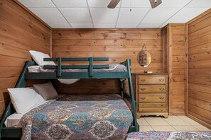 Un lit superposé avec une couvre-lit à motifs, une commode en bois avec des tiroirs et un luminaire suspendu.