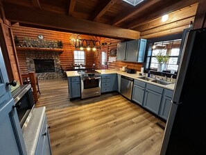 A log cabin-style kitchen with a stone fireplace, wooden floors, and a central island with a stove.