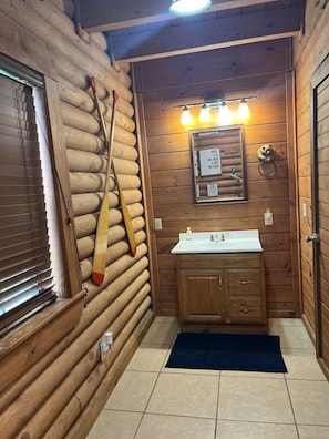 Baño de cabaña de madera con un perchero para bates de béisbol, un lavamanos y un espejo.