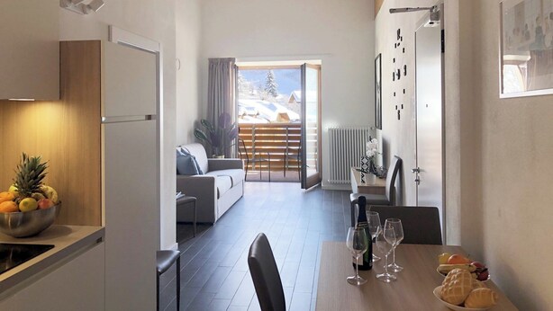 Eine moderne Küche mit Essbereich, ein Wohnzimmer mit Blick auf eine verschneite Landschaft und eine Holzbalkendecke.