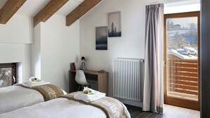 Ein Schlafzimmer mit zwei Betten, einem Schreibtisch, einem Stuhl, einem Heizkörper und einem Fenster mit Blick auf eine verschneite Landschaft.