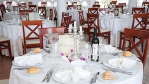 A round dining table with white tablecloths, wooden chairs, and neatly set tableware. - Hotel Il Tempio (Casal Velino)