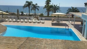 A pool area with lounge chairs and umbrellas, a clear view of the sea, and palm trees. - Hotel Il Tempio (Casal Velino)