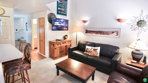 A living room with a black leather sofa, wooden coffee table, and a dining area with a white table and chairs. - The Tumbleweed at Solano (Moab)