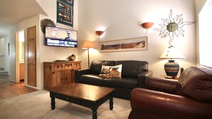A living room with a leather sofa, a wooden coffee table, and a television mounted on the wall. - The Tumbleweed at Solano (Moab)