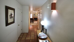 A hallway with a framed picture on the left, a table with papers and a lamp on the right, and a door at the end. - The Tumbleweed at Solano (Moab)