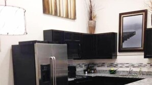 A modern kitchen with black cabinetry, a stainless steel refrigerator, and a granite countertop. - Moab Oasis Entire Condo (Moab)
