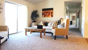A spacious living room with a large sliding glass door, a sofa set, a coffee table, and a potted plant. - Moab Oasis Entire Condo (Moab)