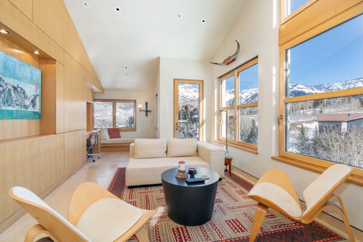 A modern living room with a sofa, two chairs, a coffee table, and large windows offering a mountain view.