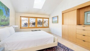 Een slaapkamer met een bed, een raam met uitzicht op gebouwen, een dakraam en een houten garderobe.
