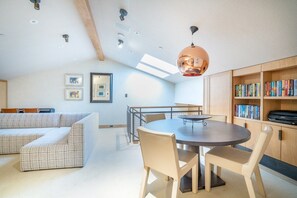 A modern living room with a sofa, dining table, chairs, and a bookshelf.