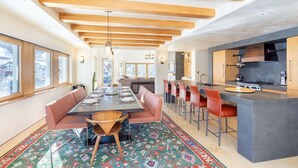 Una cocina moderna con una isla central, asientos tipo bar y un área de comedor con alfombra estampada.