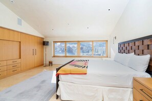 A bedroom with a large bed, wooden wardrobe, and a view of a snowy landscape through the window.