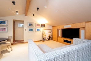 A cozy living room with a large TV, a sofa, a dining table, and artwork on the walls.