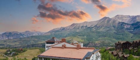 Um hotel com vários andares, área de piscina, montanhas ao redor e um campo de golfe.