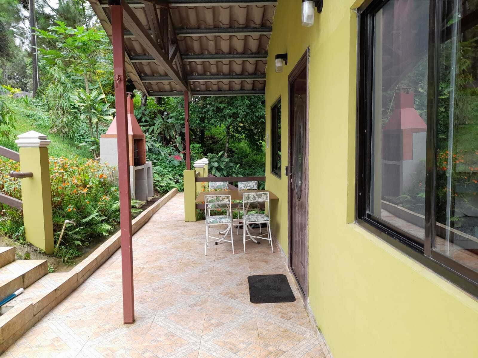 A covered patio with a tiled floor, a small table with chairs, and a view of a lush garden.