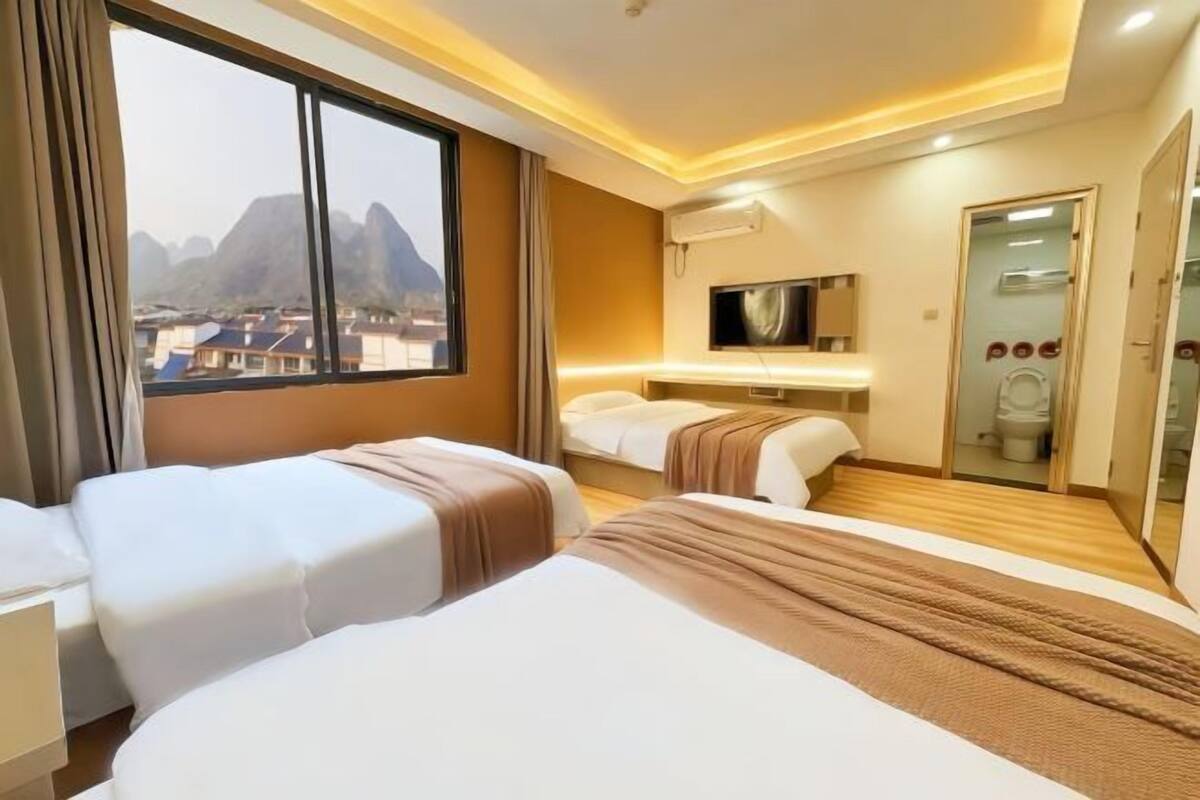 Quarto de hotel com duas camas, televisão, espelho e vista para montanhas.
