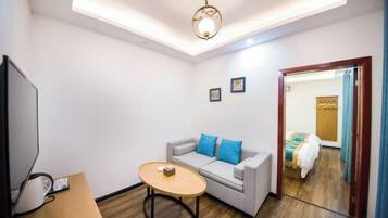 A compact room with a sofa, a small table, a television, and a ceiling light fixture.