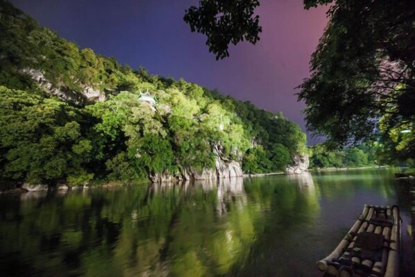 A calm river with a boat docked on the right, surrounded by dense greenery and a cliff. - Guilin Eiffel Hotel (Xiangbishan Liangjiang Sihu Branch) (Guilin)