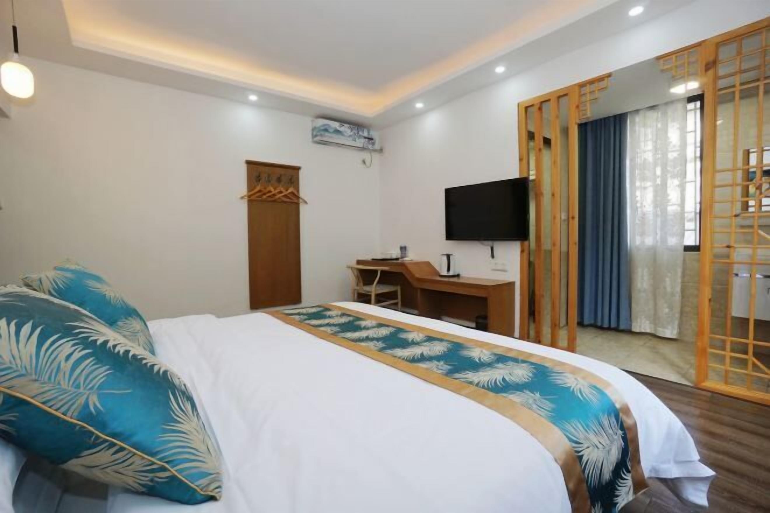 A hotel room with a bed, desk, chair, TV, and a sliding door.