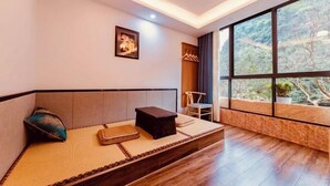 Ein Zimmer mit einem Bett, einem kleinen Tisch, einem Stuhl und einem großen Fenster mit Blick auf Bäume.