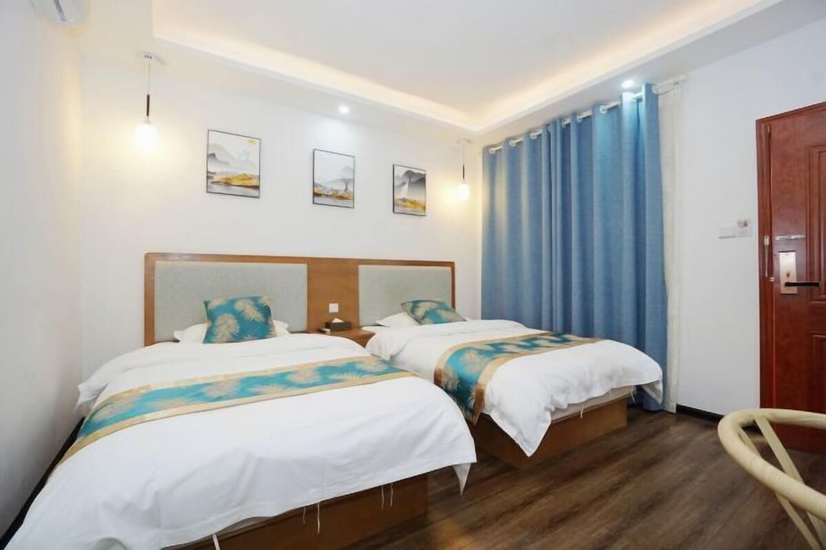 A hotel room with two single beds, a wooden headboard, a wooden floor, a wooden door, and a blue curtain.