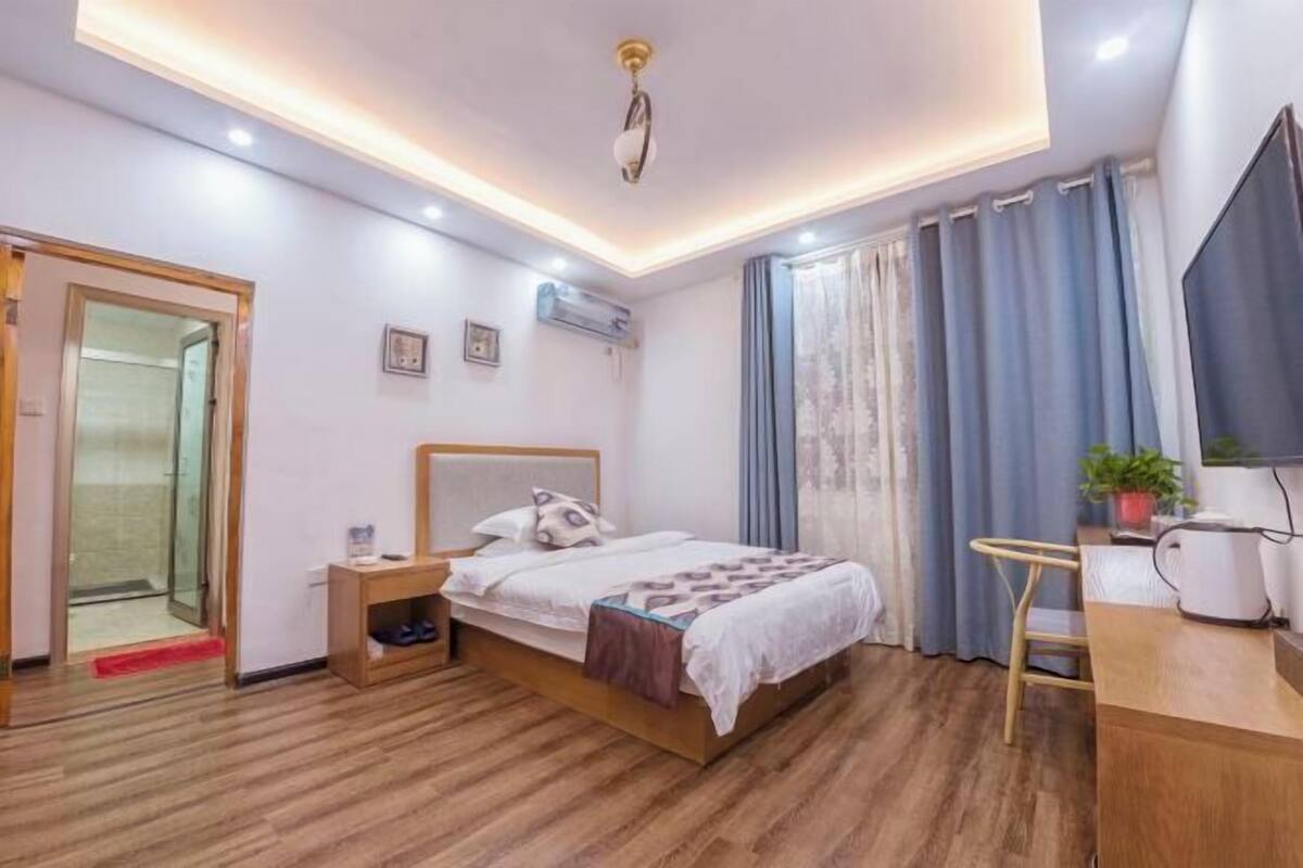 Quarto com cama, mesa de cabeceira, escrivaninha, cadeira e janela com cortinas.