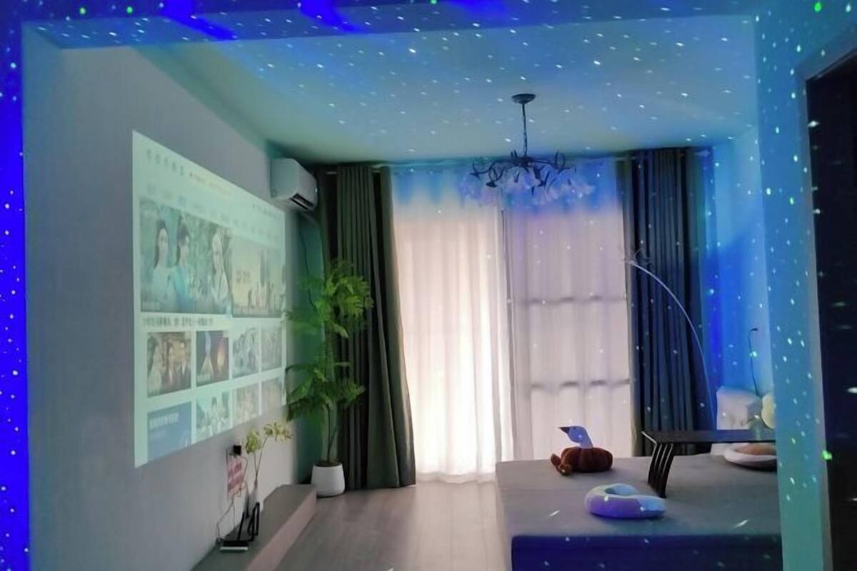 Quarto com tela de projetor exibindo imagens, planta em vaso, sofá e luminária no teto.