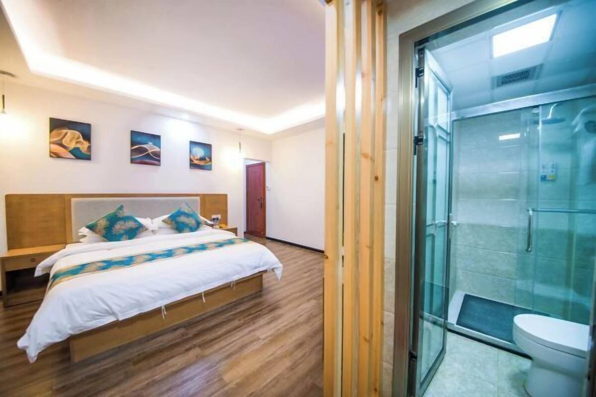 Quarto com cama de madeira, box de vidro e porta que dá para outro cômodo.