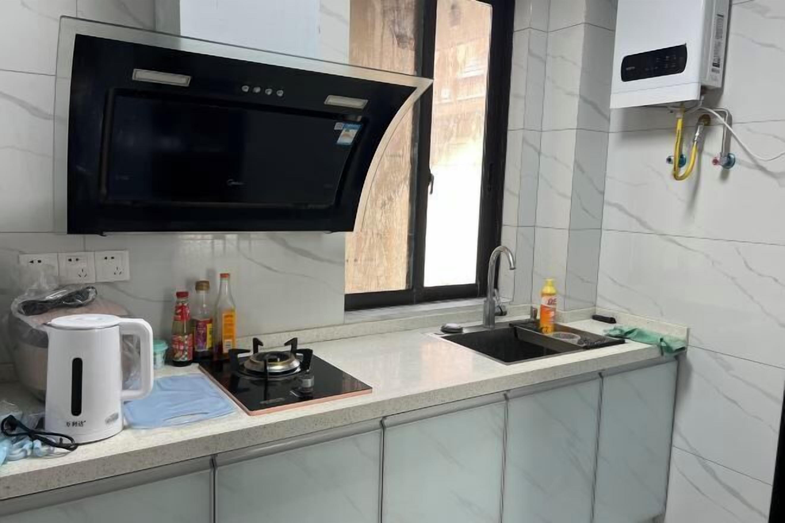 Una cocina moderna con microondas integrado, estufa a gas y lavamanos. Hay armarios, un hervidor y varios utensilios de cocina sobre la encimera.