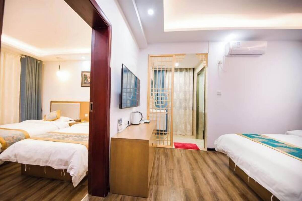 Quarto de hotel com duas camas, uma mesa, uma televisão e um ar condicionado.