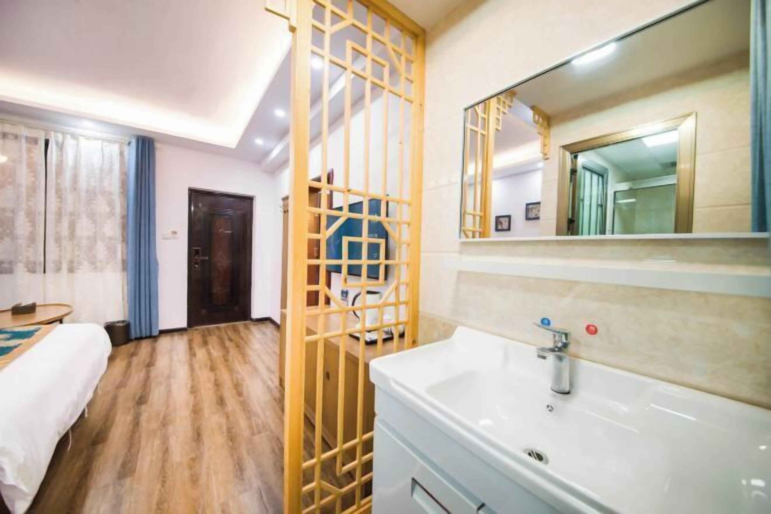 Une chambre d’hôtel avec un plancher en bois, un lit, un lavabo blanc et un miroir au-dessus.
