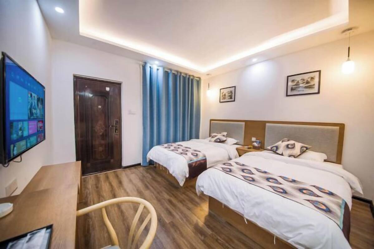 Quarto de hotel com duas camas, uma escrivaninha, uma cadeira, uma televisão e uma porta.