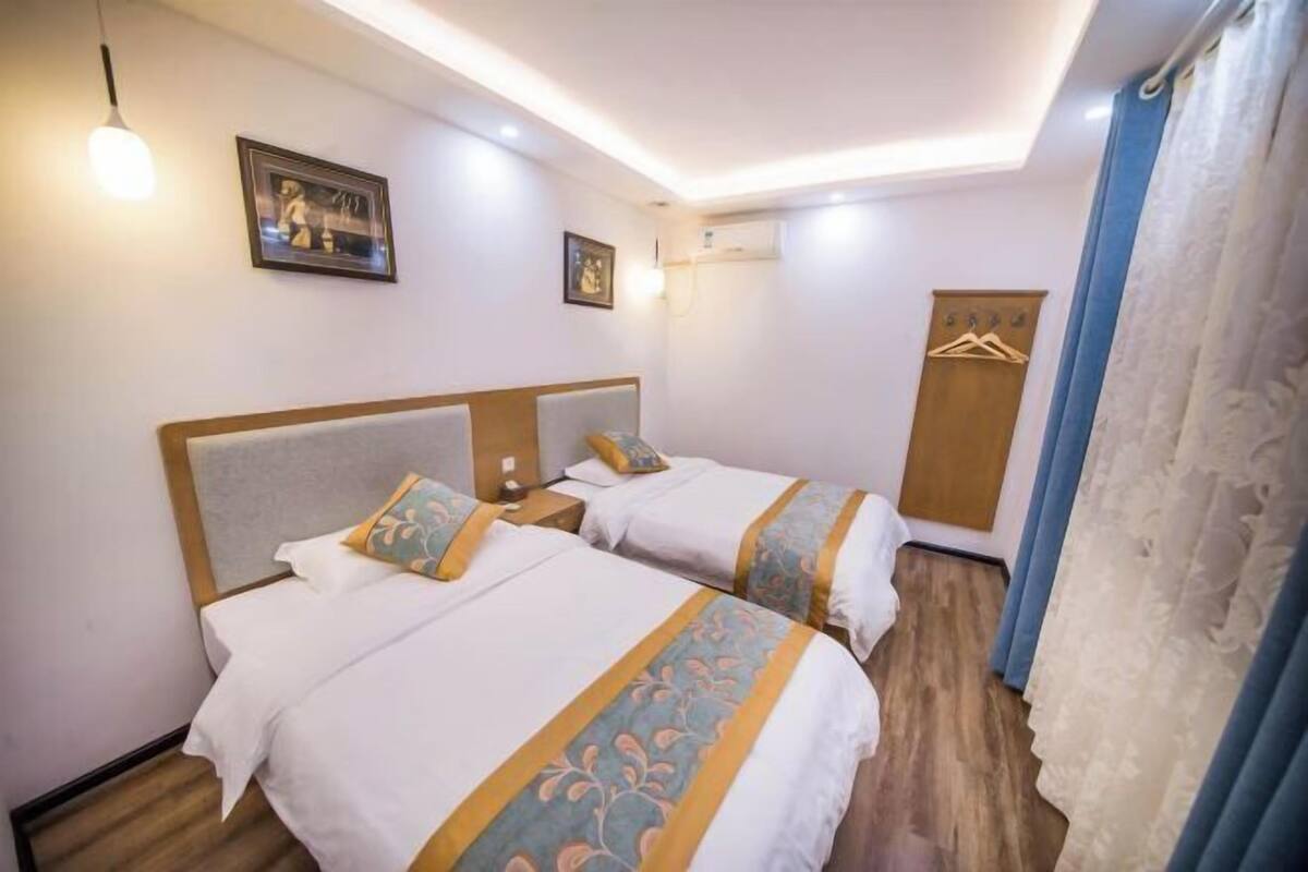 Quarto de hotel com duas camas, um guarda-roupa, um cabideiro e um candeeiro no teto.