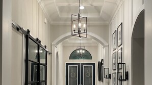 Um corredor com piso de madeira, um banco, um candelabro e portas duplas.