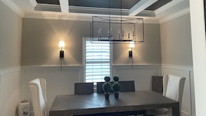 Uma sala de jantar com mesa de madeira, duas cadeiras, um lustre e luminárias fixadas na parede.