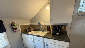 A kitchen with white cabinets, a double sink, a coffee maker, and a fire extinguisher.